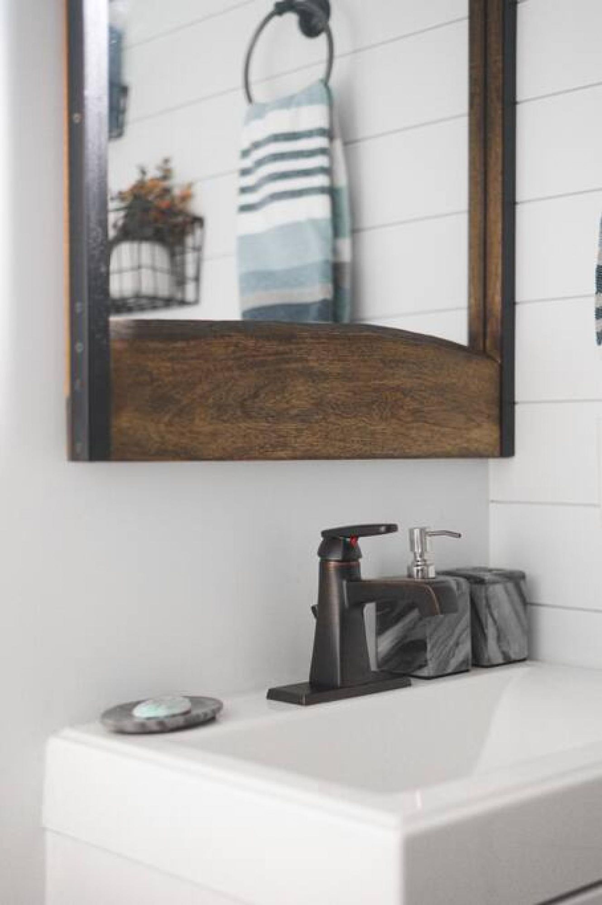 A bathroom with a white sink, a black faucet, and a wooden-framed mirror.