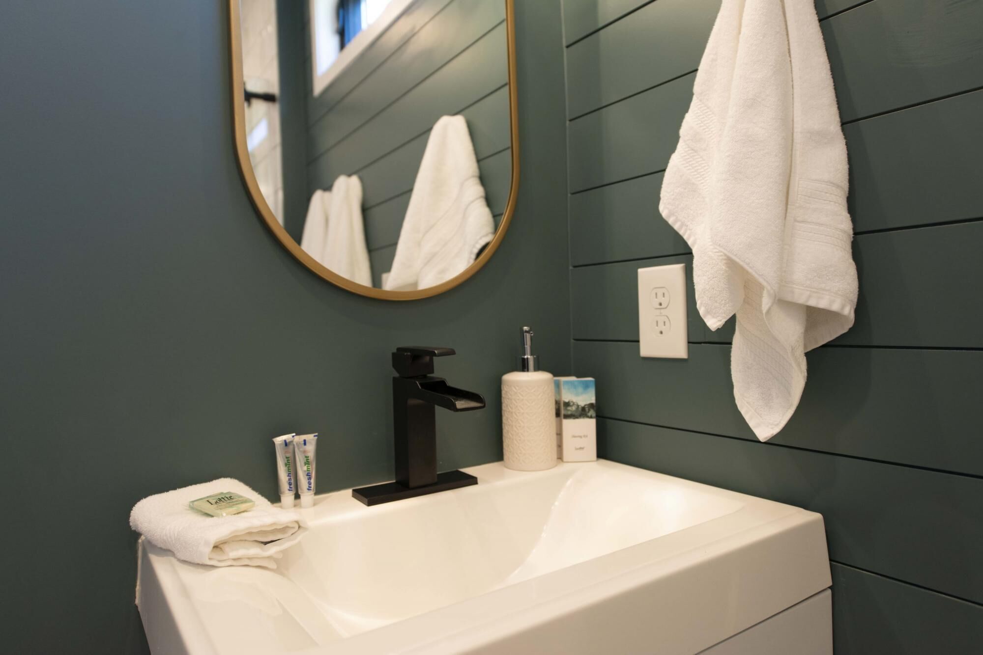 A bathroom with a white sink, a black faucet, a mirror, and a towel hanging on the wall.