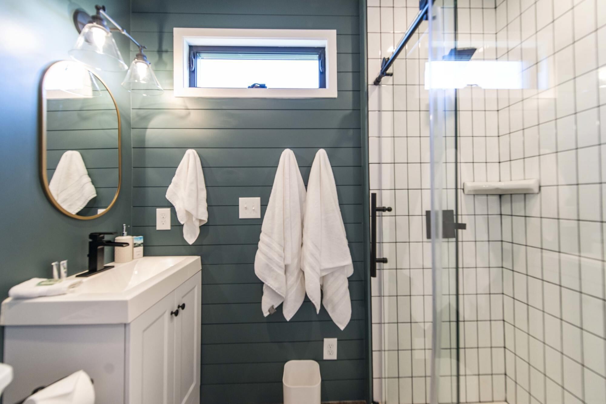 A bathroom with a dark green wall, a white sink, a mirror, and two towels hanging on the wall.