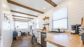 A modern kitchen with wooden beams, white walls, and a wooden countertop. - The Meadows Container Home in Country Setting (Waco)