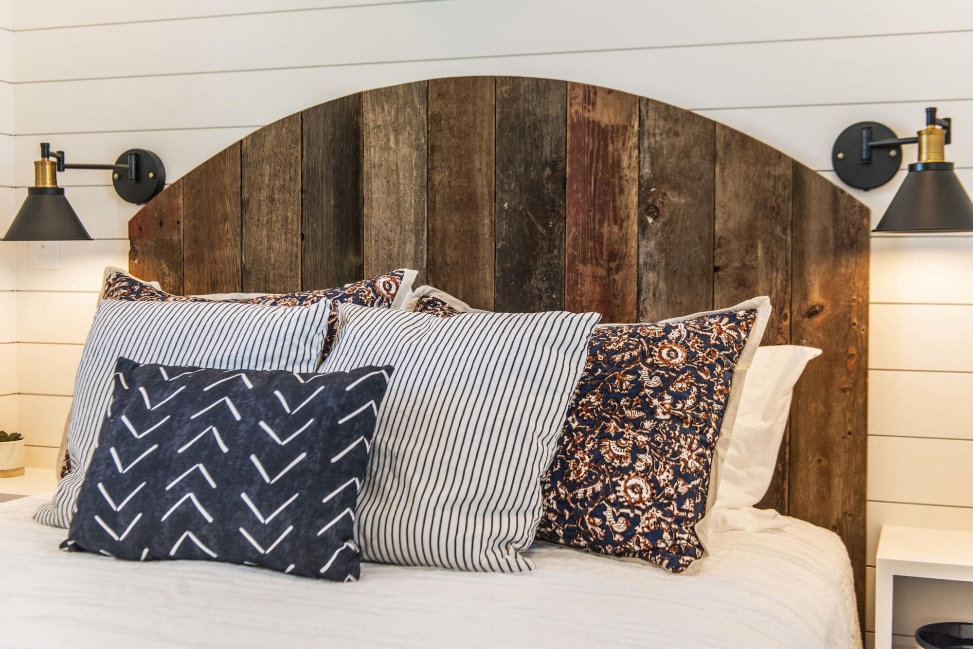 A bed with a wooden headboard, striped pillows, and two wall-mounted lamps.