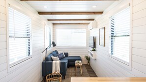 A cozy, well-lit room with a blue sofa, a small wooden table, and a wicker basket. - The Meadows Container Home in Country Setting (Waco)