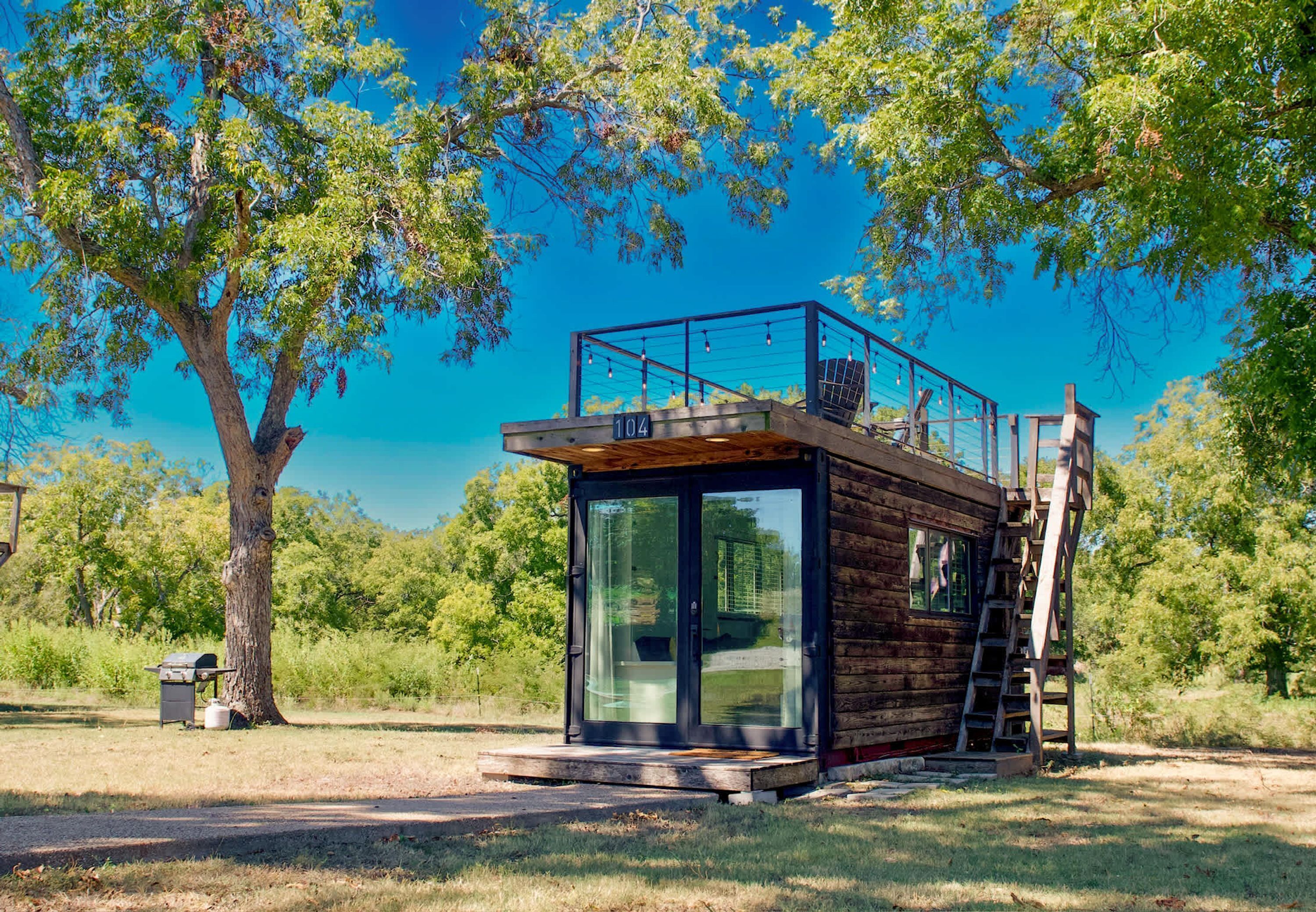 Una cabaña moderna con puerta de cristal, terraza de madera y barandilla metálica.
