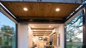 A modern interior with a wooden ceiling, a kitchen area, and a seating area with a sofa and cushions. - Yellow Blue Elegant Container Tiny House (Waco)