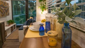 A modern kitchen with a wooden countertop, a dining area with a sofa, and a window with blinds. - Yellow Blue Elegant Container Tiny House (Waco)