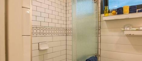 A small, enclosed shower area with a glass door, white tiled walls, and a window above the sink.