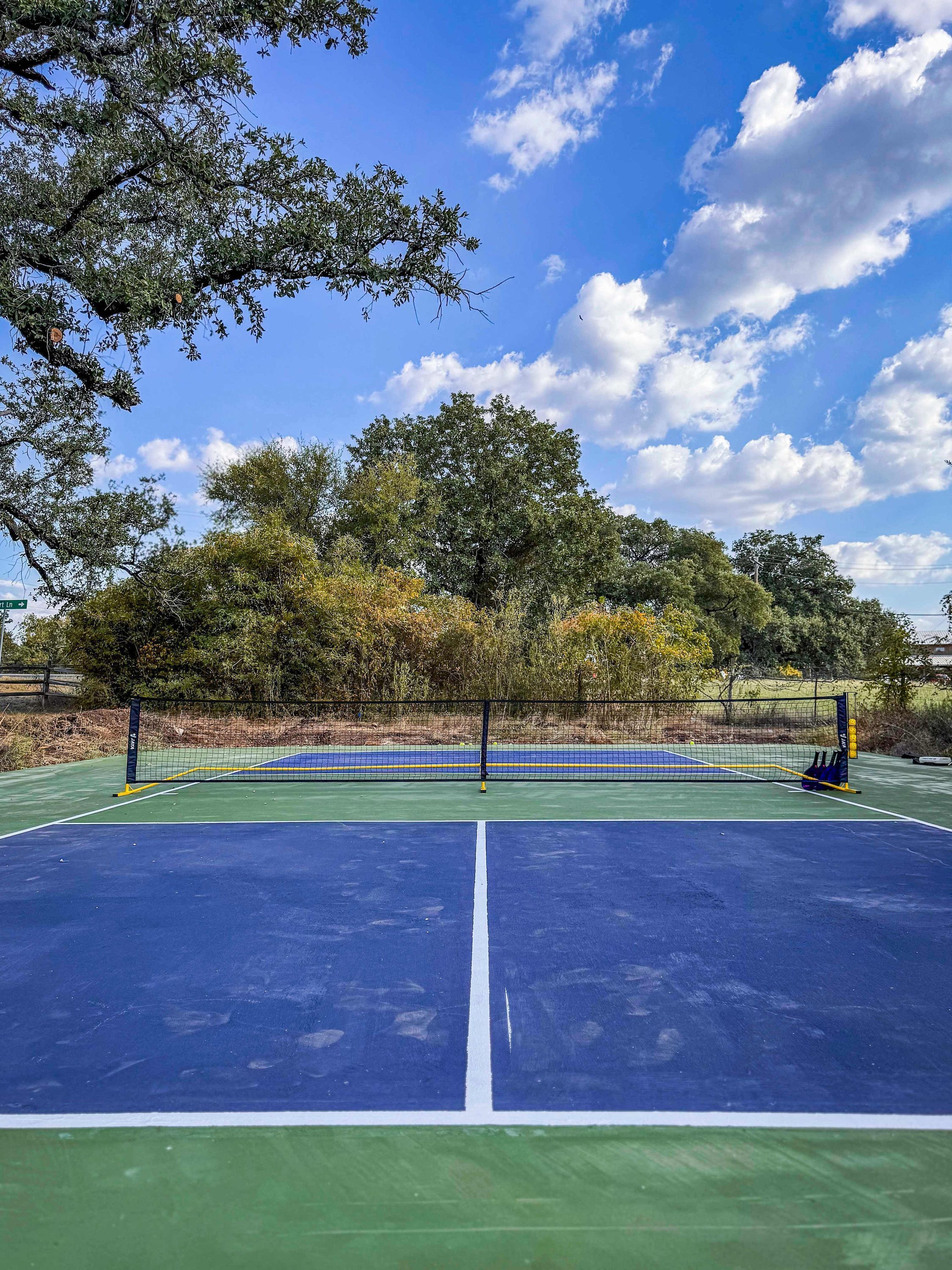 An outdoor tennis court with a net, surrounded by trees and a clear sky.