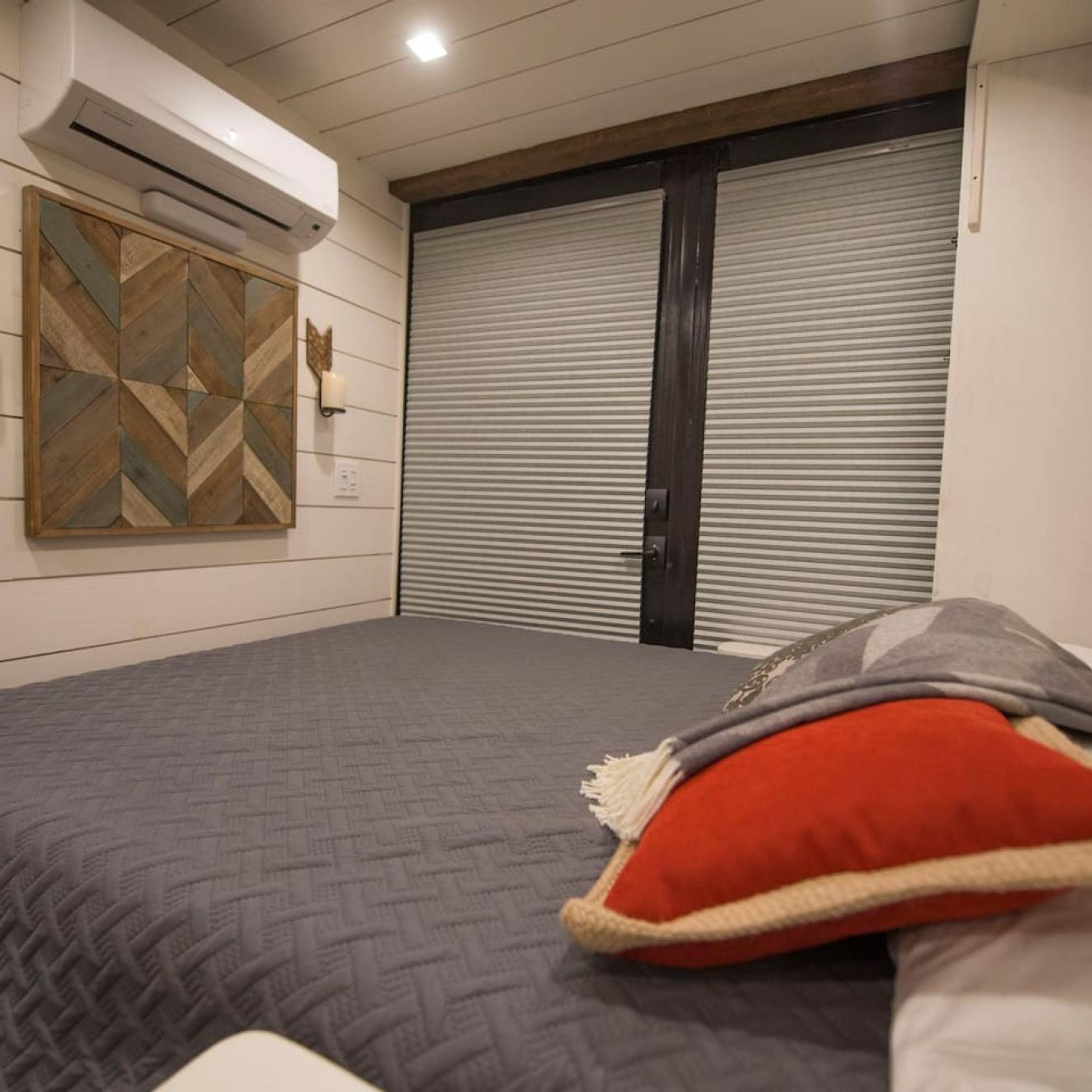 A bedroom with a bed, a wall-mounted air conditioner, a geometric wall art piece, and a closed sliding door.