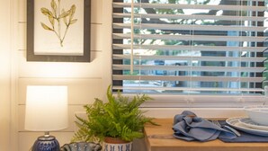Un coin repas avec une table en bois, une plante en pot, un bol décoratif et une illustration botanique encadrée accrochée au mur.