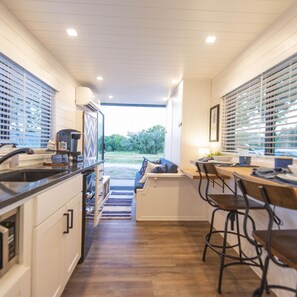 A modern kitchen with a central island, bar seating, and a view of the outdoors. - The Bluebonnet- Container Home Country Setting Near Waco Attractions (Waco)