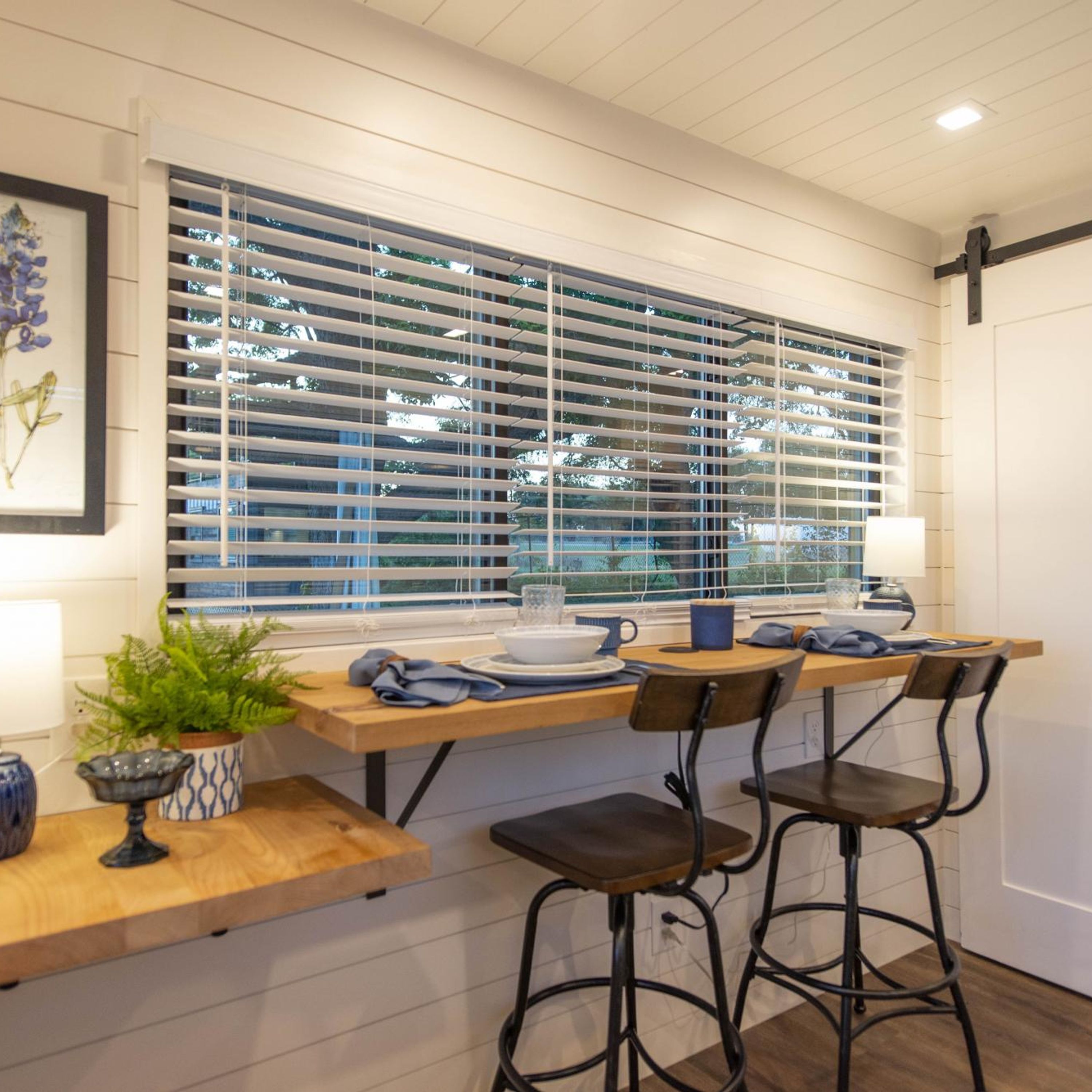 A modern kitchen with a wooden countertop, bar stools, and a window with blinds.