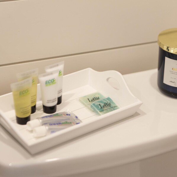 A bathroom sink with toiletries including ECO body lotion, Lottie's soap, and a candle.