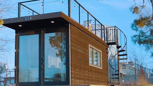 Une cabane moderne avec une façade en verre, un revêtement extérieur en bois et un escalier en métal.