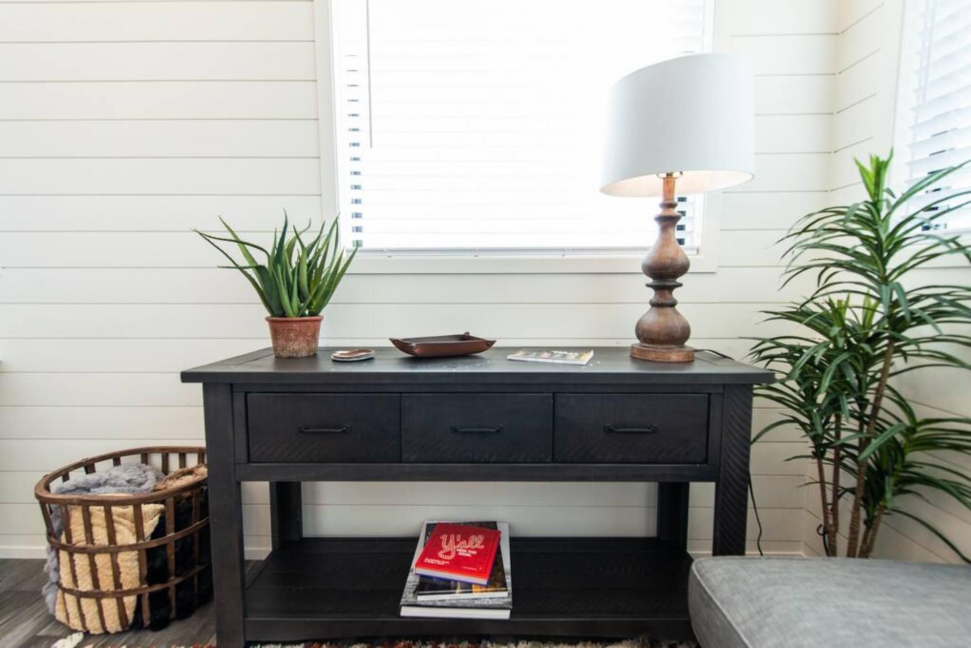Une console en bois foncé, ornée d’une lampe, d’une plante en pot et d’un panier.
