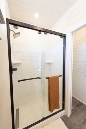 A modern bathroom with a glass shower enclosure, white tiled walls, and a visible towel rack.
