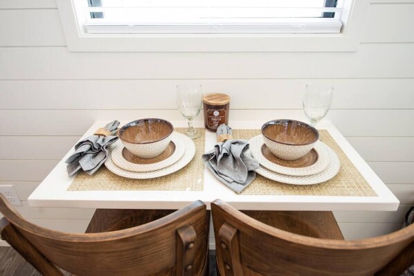 A dining table with two sets of bowls and plates, a candle, and glasses on a white tablecloth.