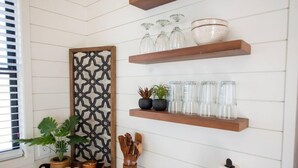 A kitchen with wooden shelves holding glassware, a decorative panel, and potted plants. - New Longhorn Stunning Container Home-in Alpine (Alpine)