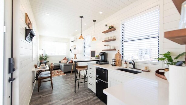 A modern kitchen with white cabinetry, a dining area with a wooden table and chairs, and a small island with a sink. - New Longhorn Stunning Container Home-in Alpine (Alpine)