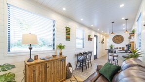 A modern living room with a wooden reception desk, a leather sofa, and a dining area with a table and chairs. - The Woods- Container Tiny House 12 min to Magnolia Baylor Downtown (Waco)