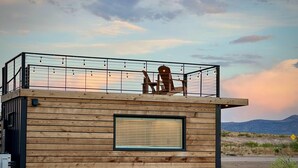 A wooden cabin with a balcony, a large window, and a chair. - New The Cowboy Boots-shipping Container Home (Alpine)