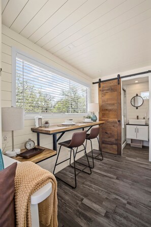 A cozy room with a wooden dining table, two chairs, a small clock, and a window with blinds. - New The Desert Escape-cozy Container Home (Fredericksburg)