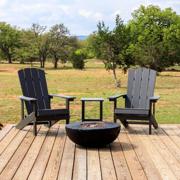 Una terraza con dos sillas Adirondack y una pequeña mesa, rodeada de un césped con árboles.