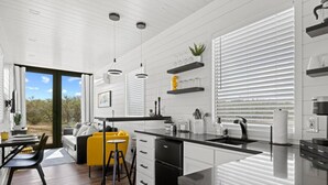 A modern kitchen with white cabinetry, a black countertop, and a dining area with a yellow chair and a sofa. - New The Yellow Beacon-luxury Shipping Container (Fredericksburg)