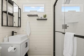 Un baño moderno con un tocador blanco, una cabina de ducha de vidrio y una ventana pequeña con vistas.