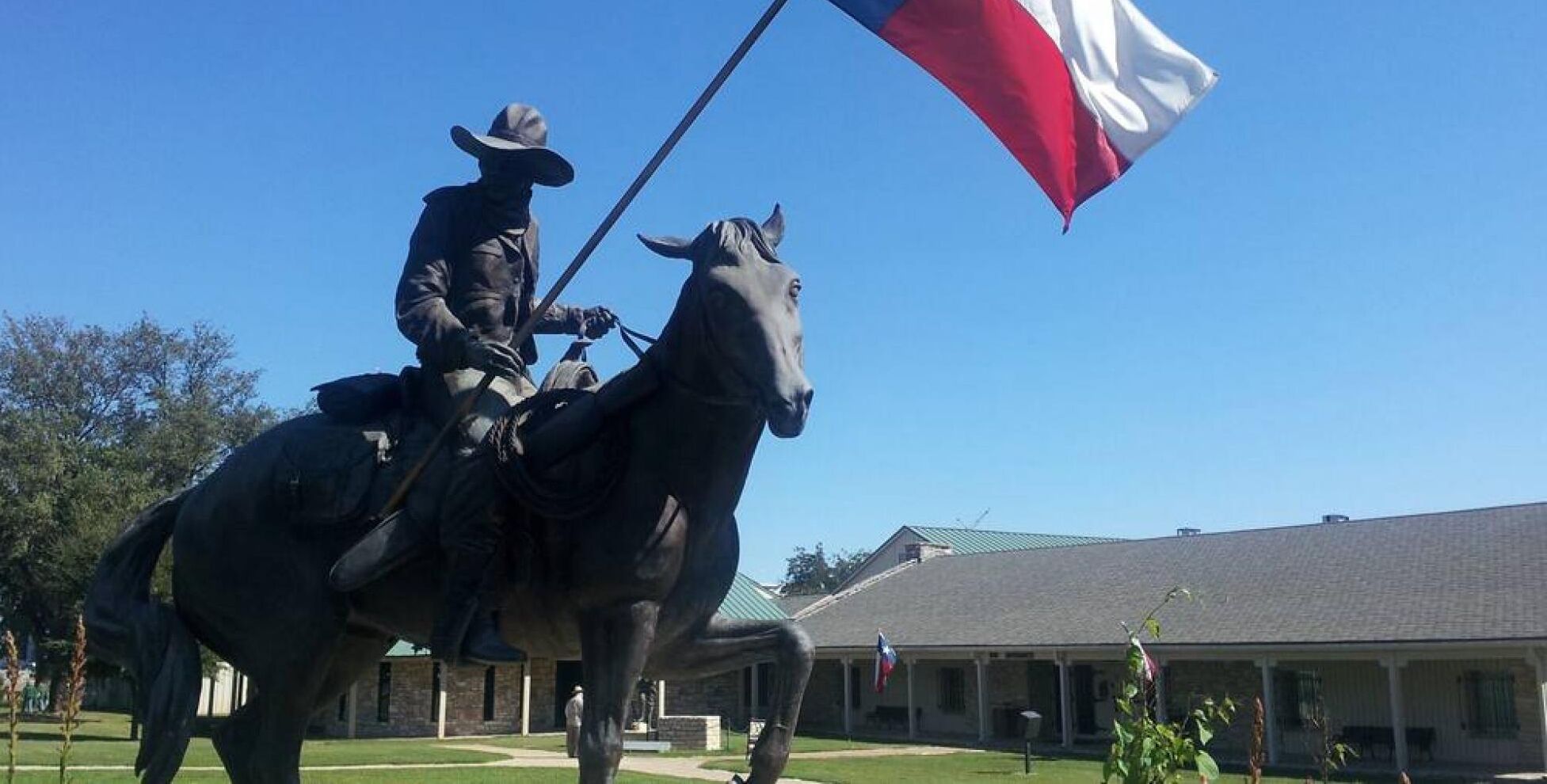 A statue of a person on horseback with a flag, set against a building with a green roof and a flagpole.