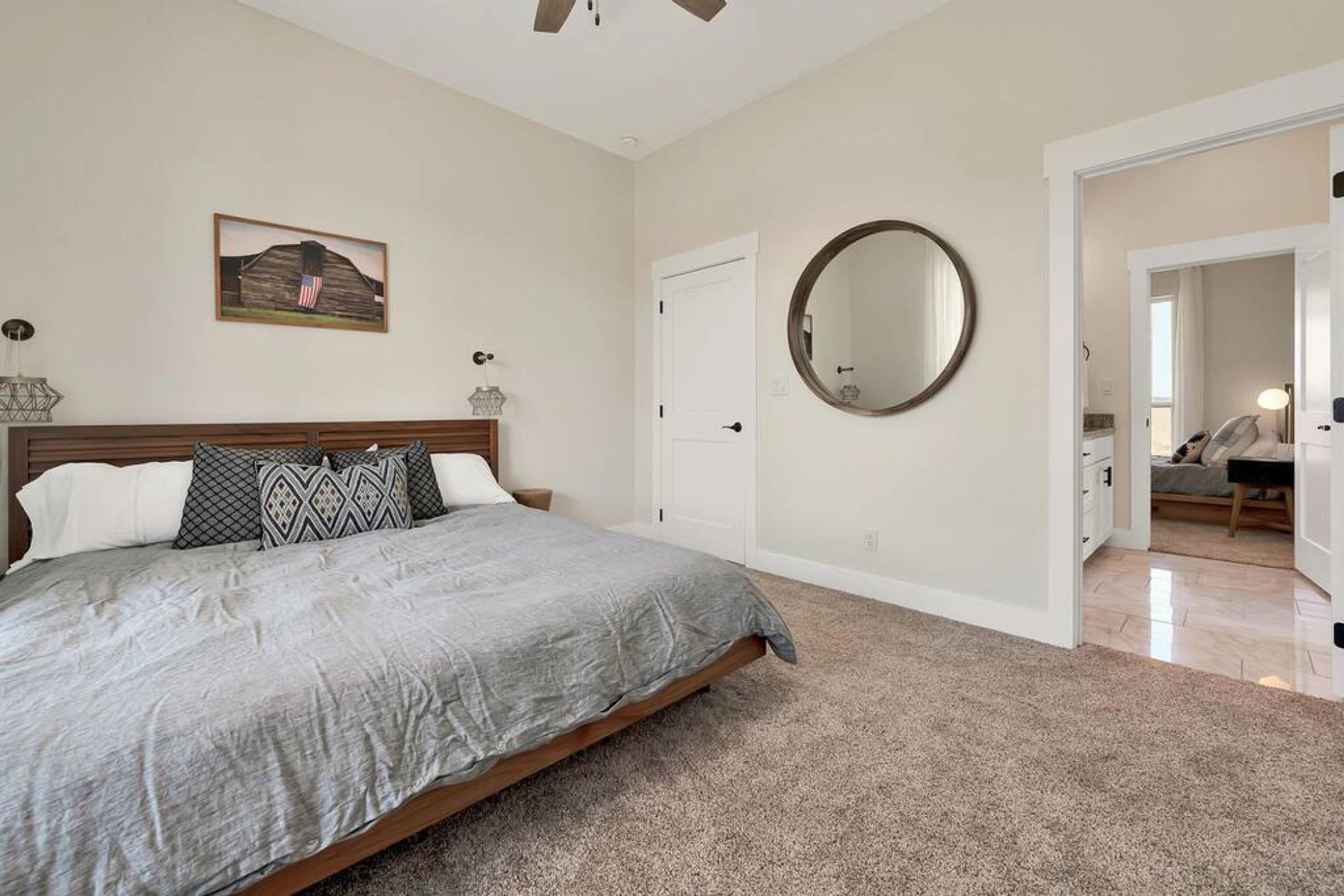 A bedroom with a bed, a round mirror, a door, and a hallway leading to another room.