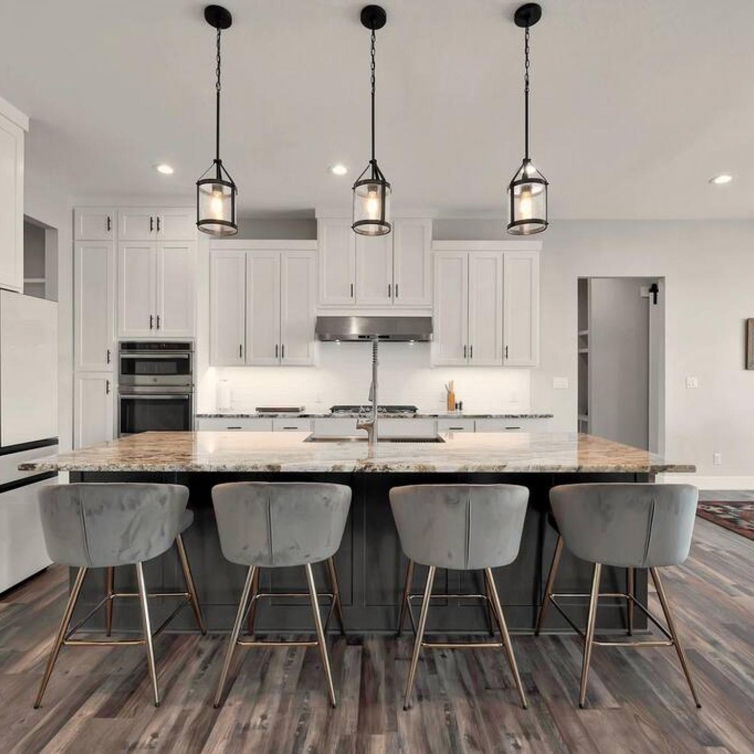 A modern kitchen with white cabinets, a marble island, and three bar stools.