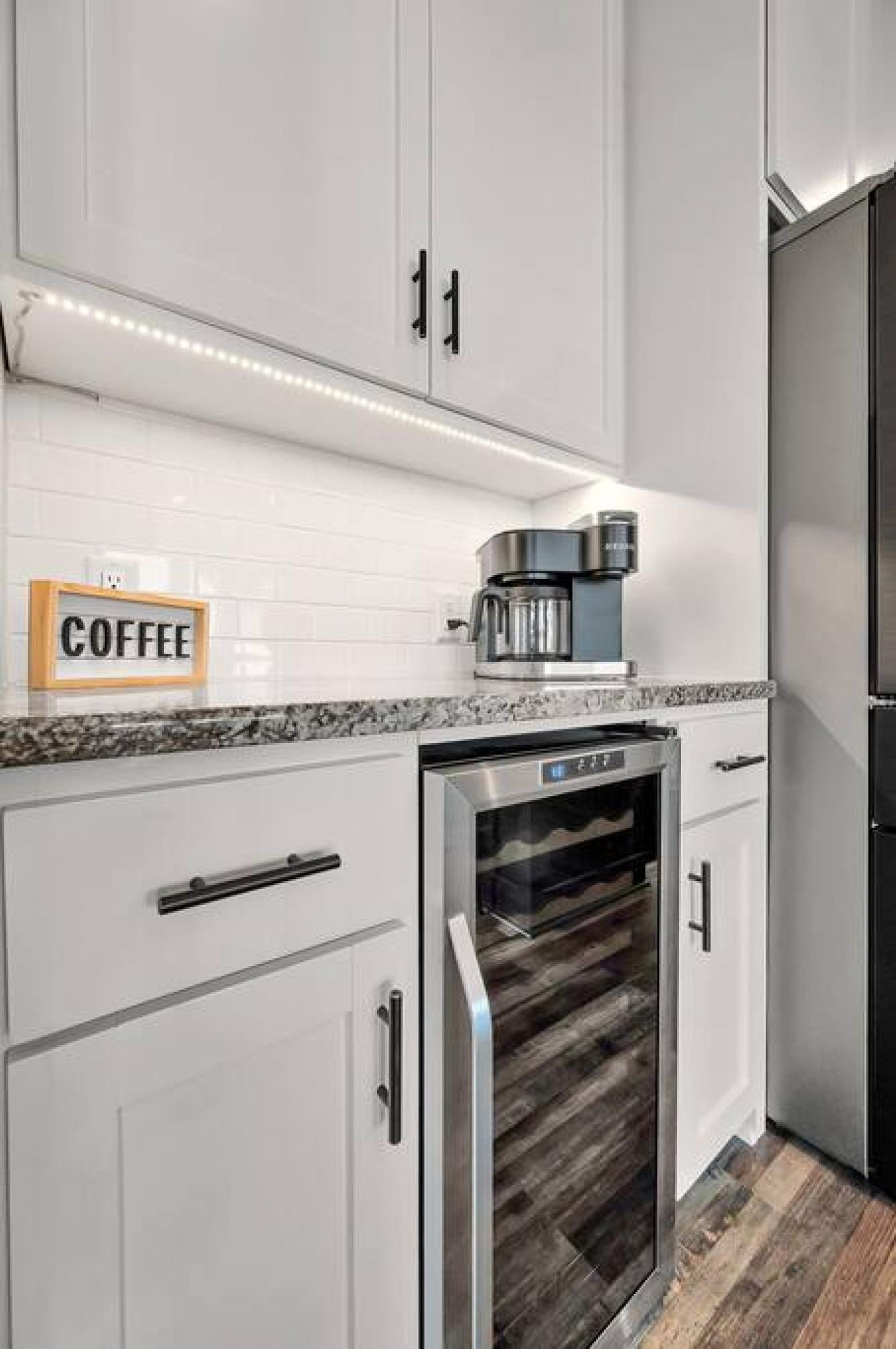 A modern kitchen with white cabinets, a built-in oven, and a coffee maker on the countertop.