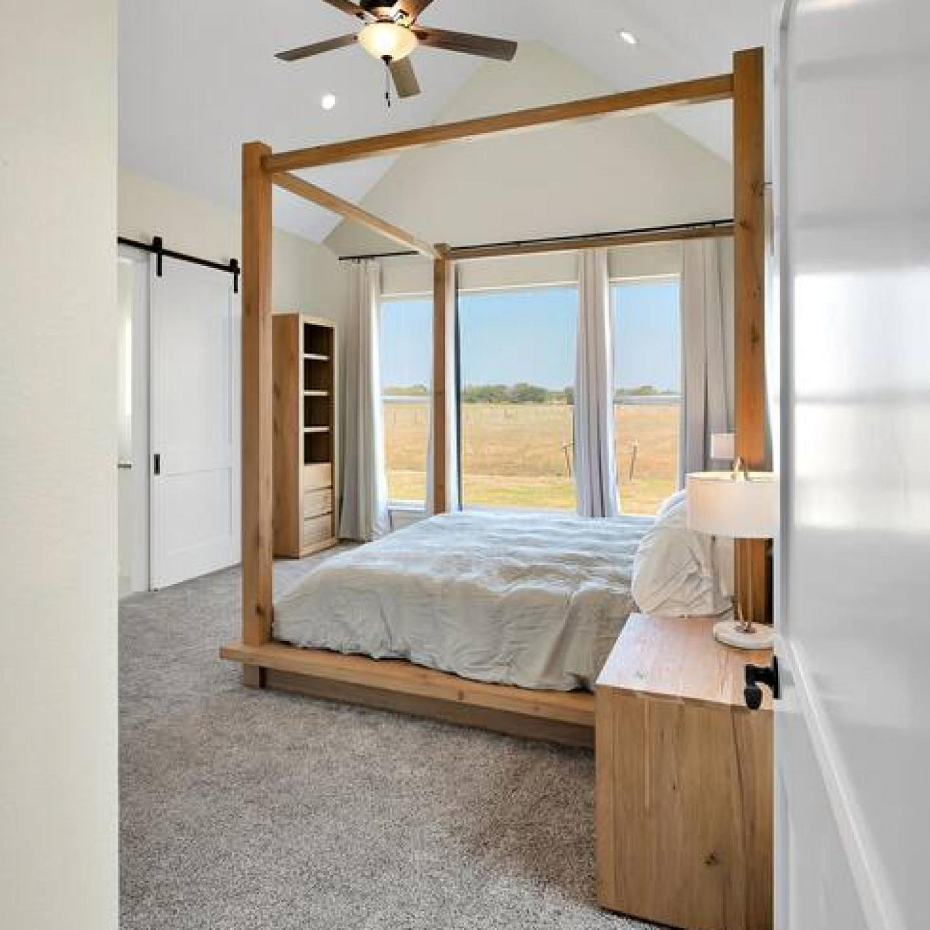 A bedroom with a four-poster bed, large windows, and a ceiling fan.