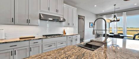 A modern kitchen with white cabinets, a granite countertop, and a stainless steel range hood.