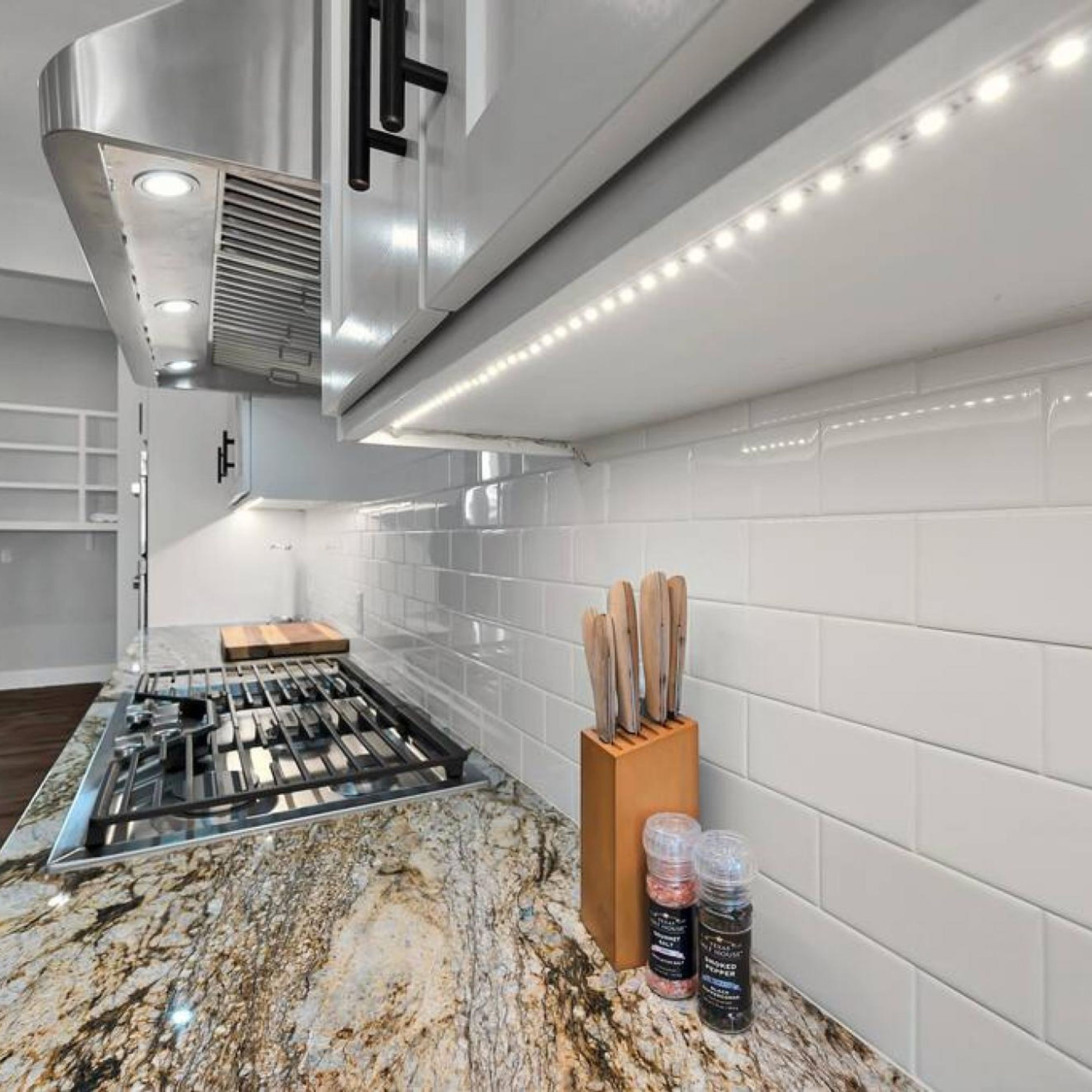 A modern kitchen with a stainless steel range hood, white subway tiles, and a granite countertop.