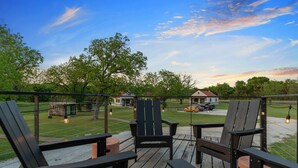 A deck with chairs and tables, overlooking a grassy area with a house and a car. - Cool River Helm Model Container Home 12 Minutes to Magnolia Baylor (Waco)