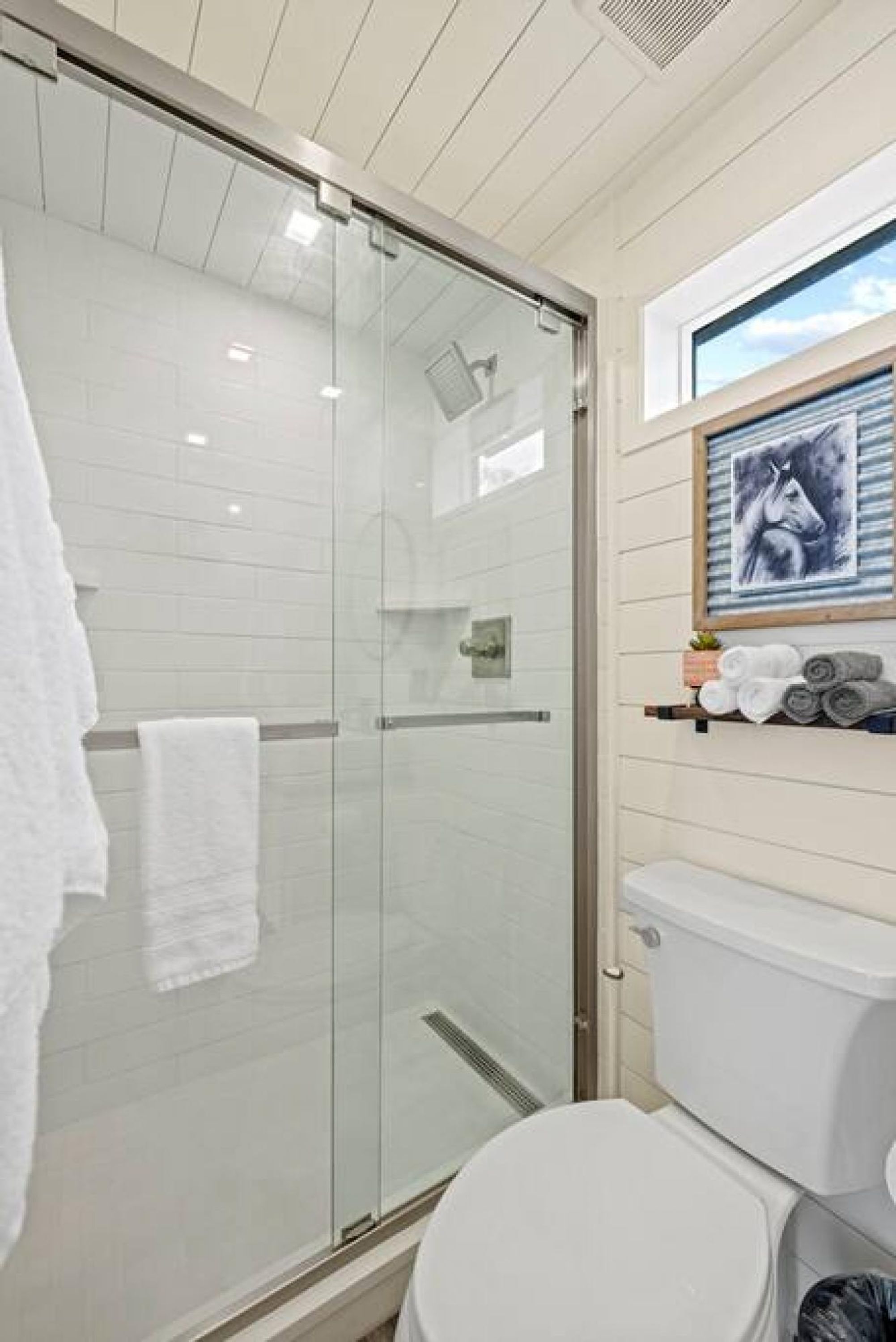 A modern bathroom with a glass shower enclosure, a toilet, and a towel rack with towels.