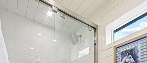A modern bathroom with a glass shower enclosure, a toilet, and a towel rack with towels.