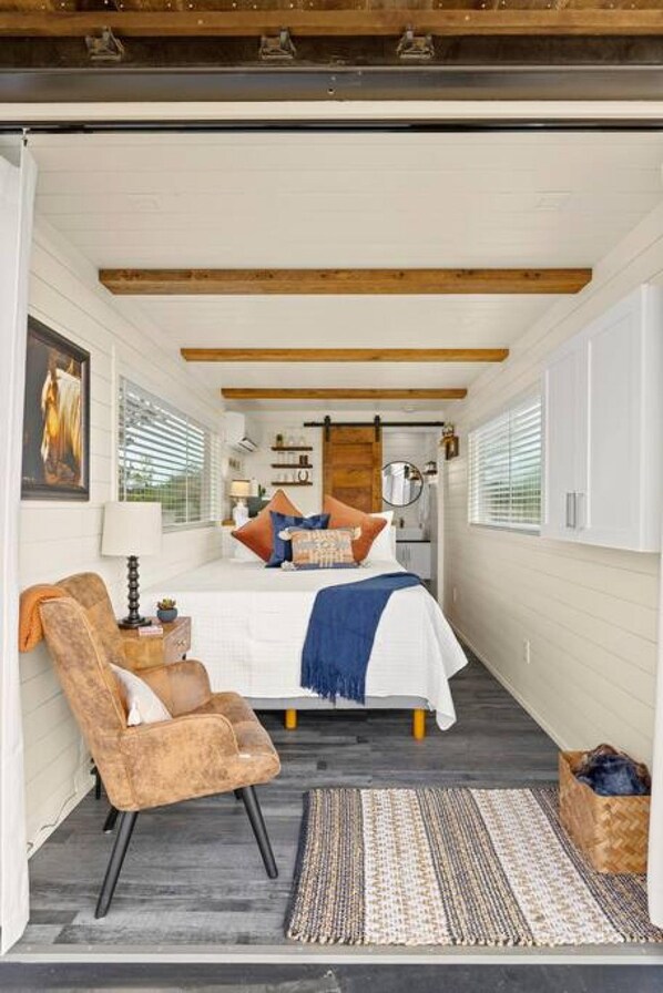 A bedroom with a bed, a chair, a bedside table, and a window.