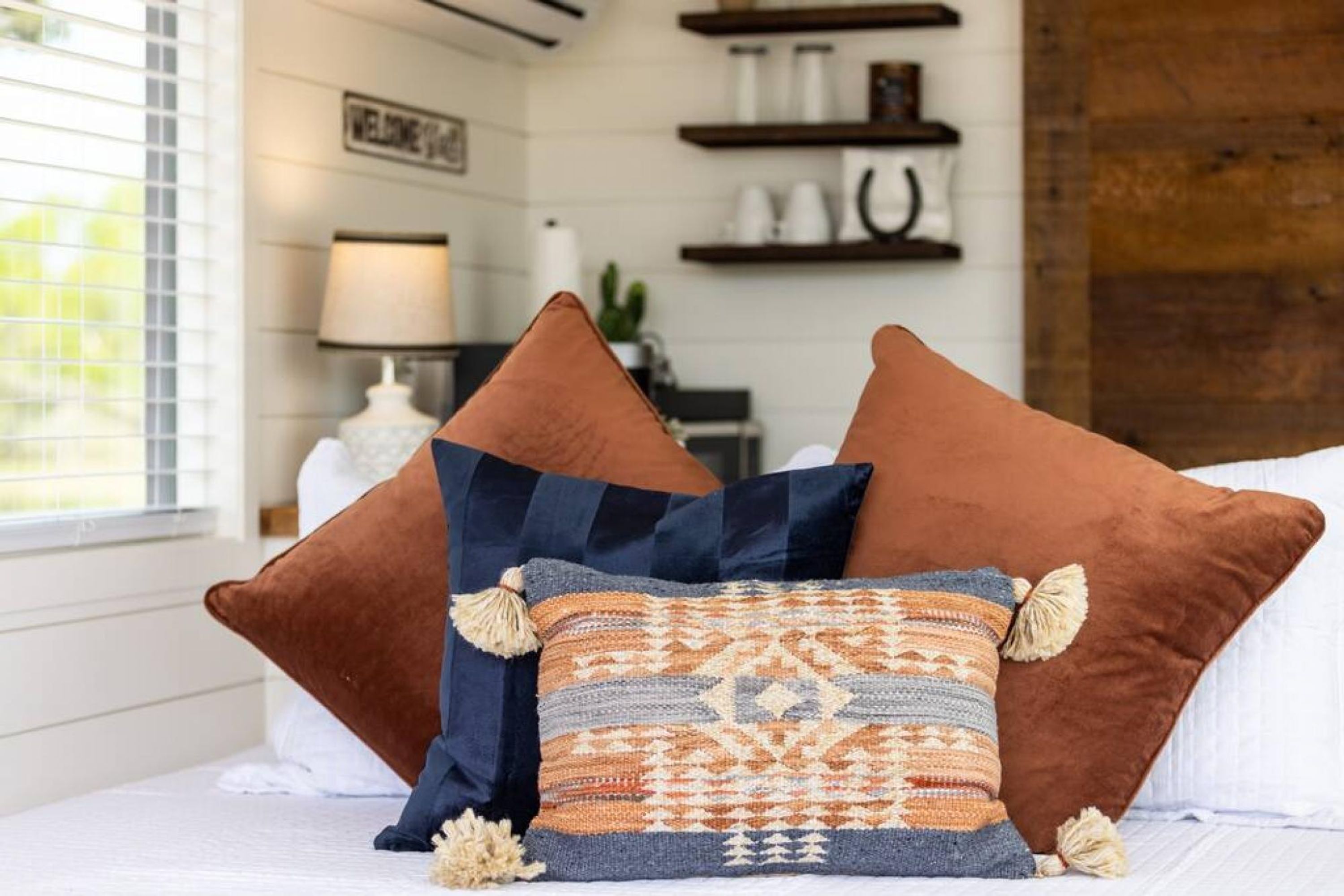 Un lit avec trois oreillers, une lampe et une étagère avec quelques objets.
