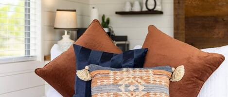 A bed with three pillows, a lamp, and a shelf with items.