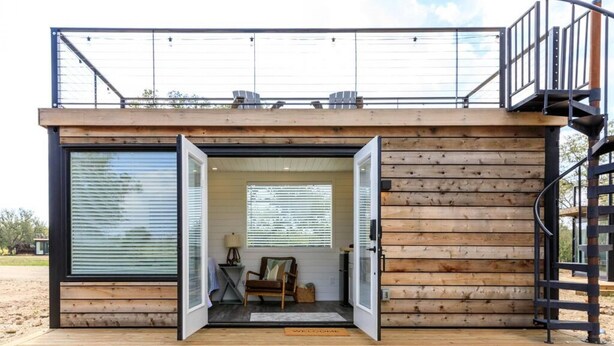 A modern cabin with a wooden exterior, a balcony, and a staircase. - New The Sunset Luxury Container Home (Fredericksburg)
