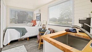 A compact bedroom with a bed, bedside table, lamp, and a view through the window. - New The Sunset Luxury Container Home (Fredericksburg)