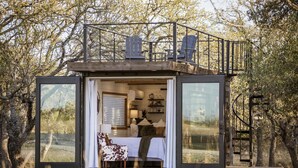A modern, compact cabin with a balcony, large windows, and a cozy interior with a bed and seating area. - New The Lone Star Shipping Container (Fredericksburg)