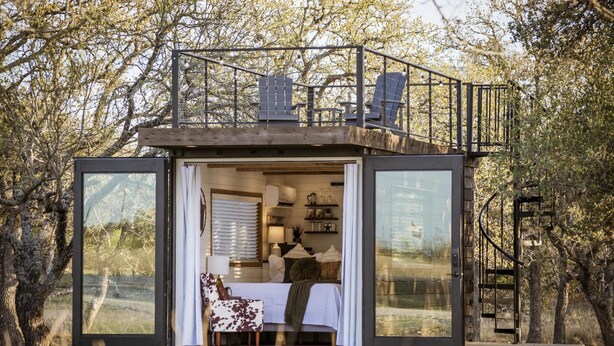 A modern, compact cabin with a balcony, large windows, and a cozy interior with a bed and seating area. - New The Lone Star Shipping Container (Fredericksburg)