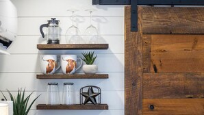 A kitchen shelf with coffee maker, glasses, mugs, and decorative items. - New The Lone Star Shipping Container (Fredericksburg)