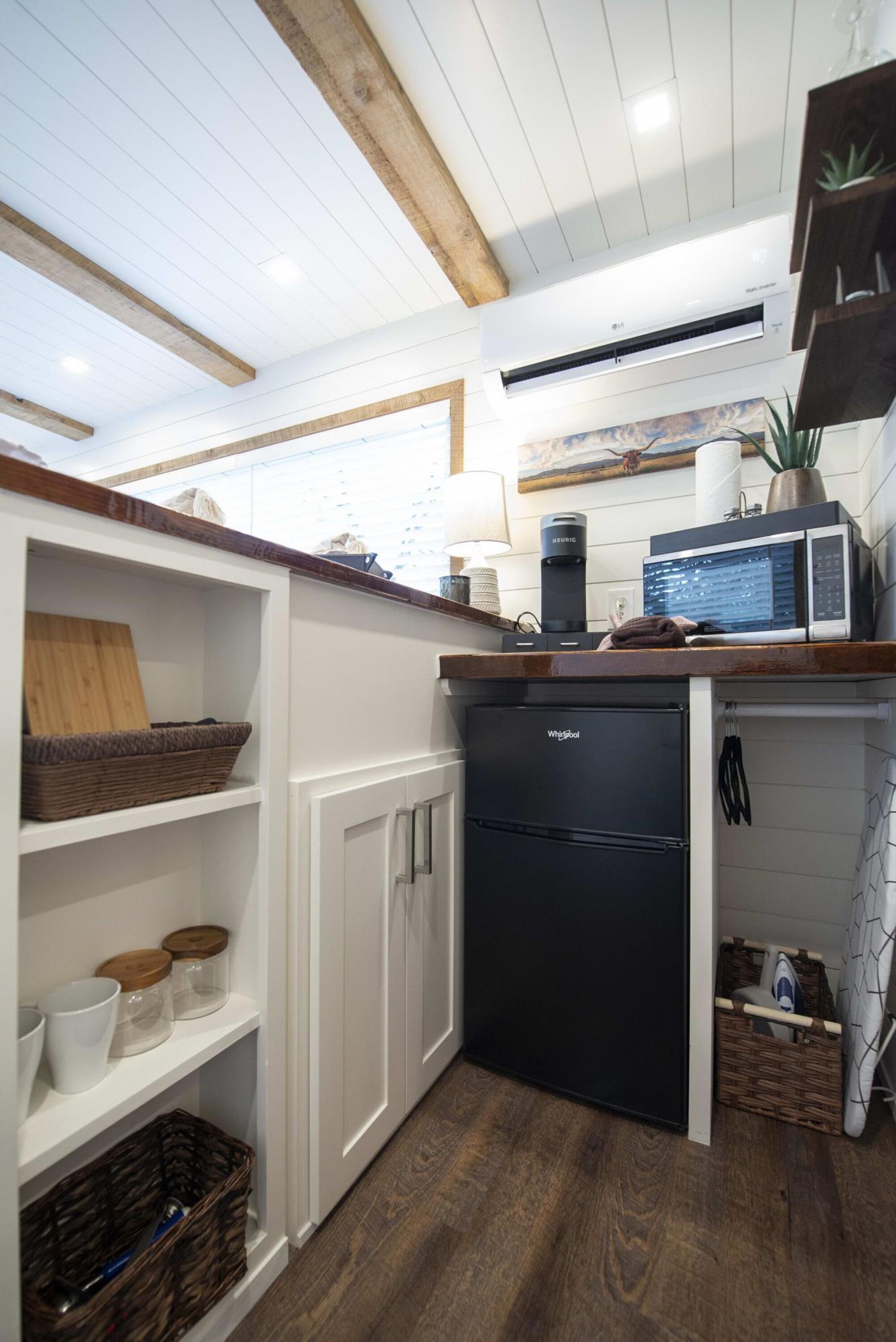 A compact kitchen with white cabinetry, a black refrigerator, a microwave, and a coffee maker on the countertop.