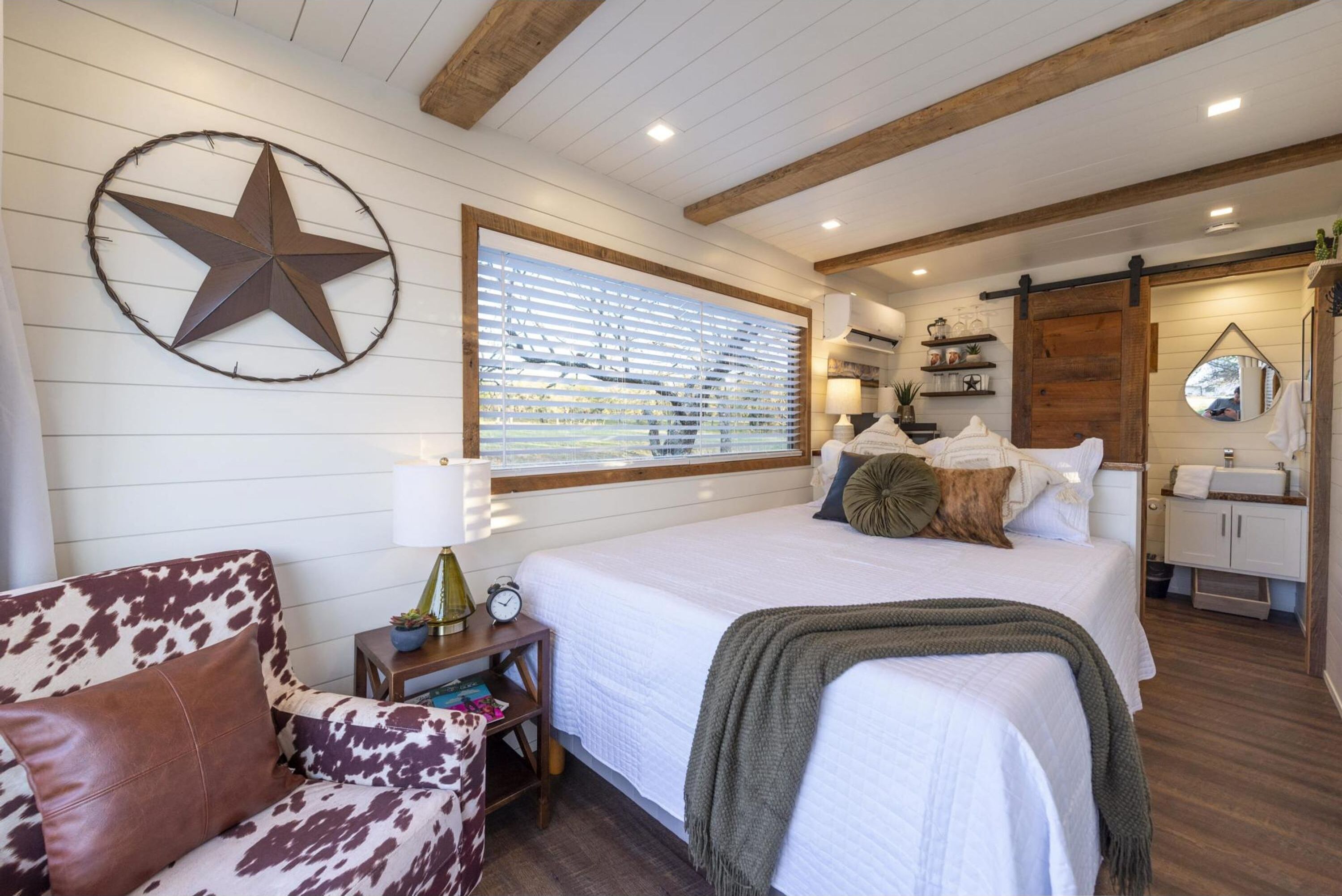 Een slaapkamer met een groot bed, een ster decoratie, een raam met zonwering, een houten plafond, een nachtkastje en een dressoir.