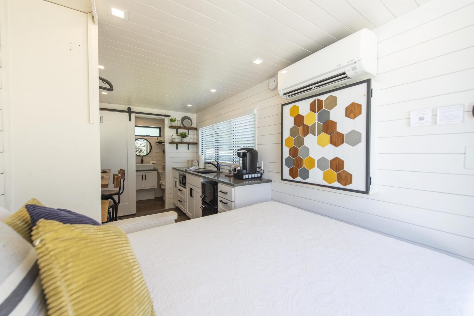 Une pièce compacte et bien éclairée, comprenant un lit, une kitchenette et une salle de bain.