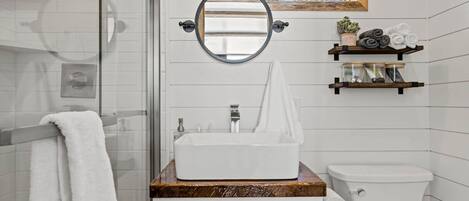 A bathroom with a white sink, a mirror, a toilet, and a shower area.